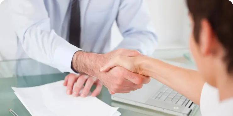 Two people shaking hands over a laptop