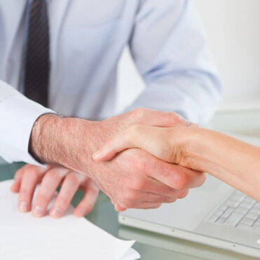 Two people shaking hands over a laptop